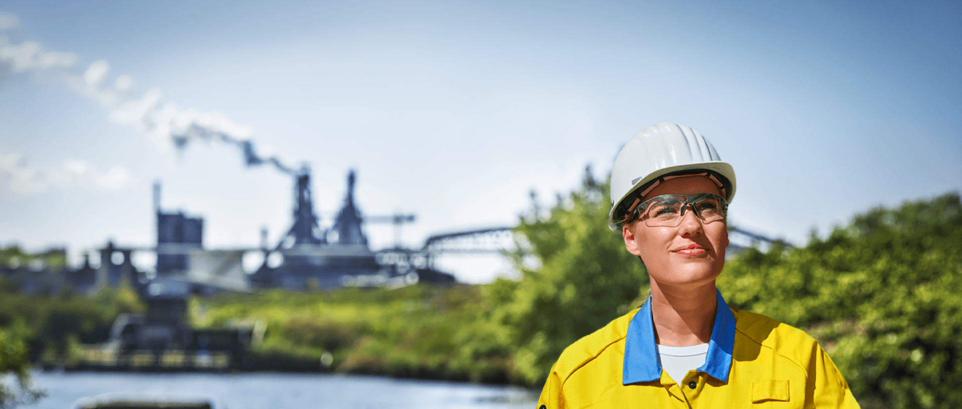 Medewerker van Tata Steel met helm en veiligheidsbril bij industrieterrein in groene omgeving.