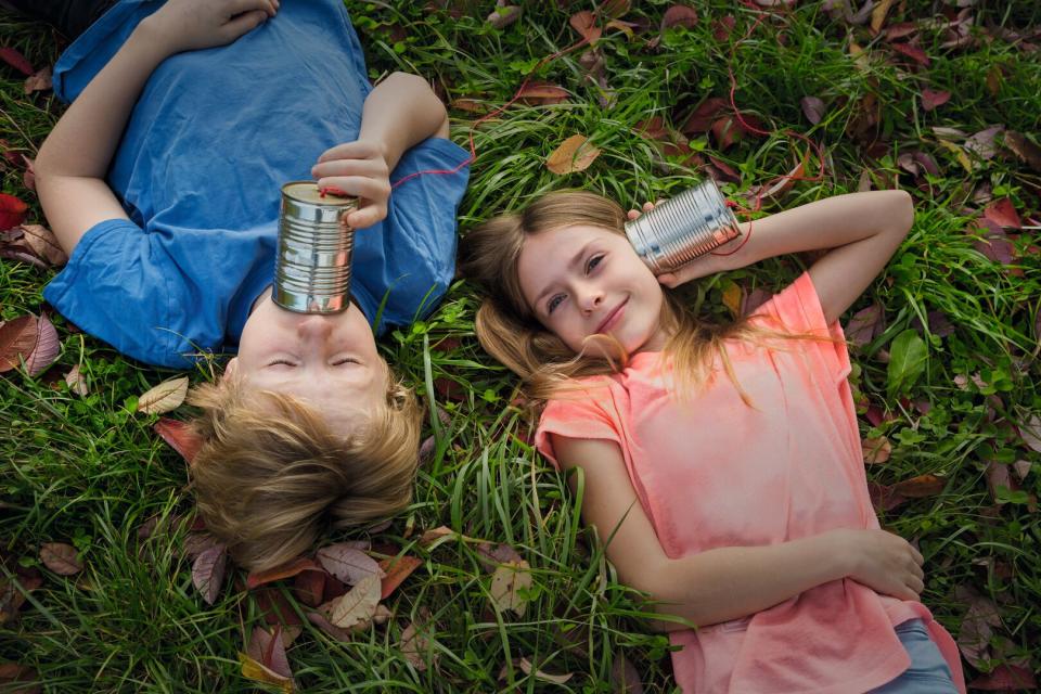 Boy and girl on a meadow having fun with tin can phone